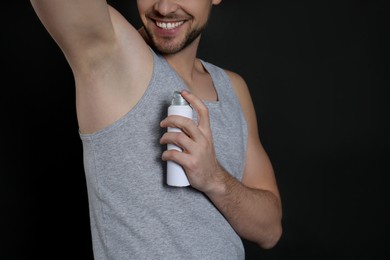 Photo of Man applying deodorant on black background, closeup