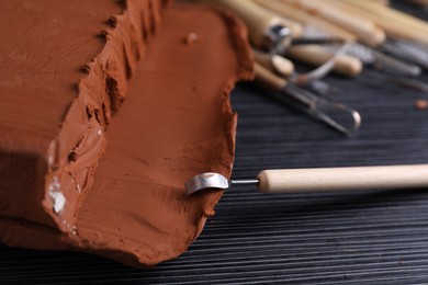 Photo of Clay and modeling tool on dark gray wooden table, closeup