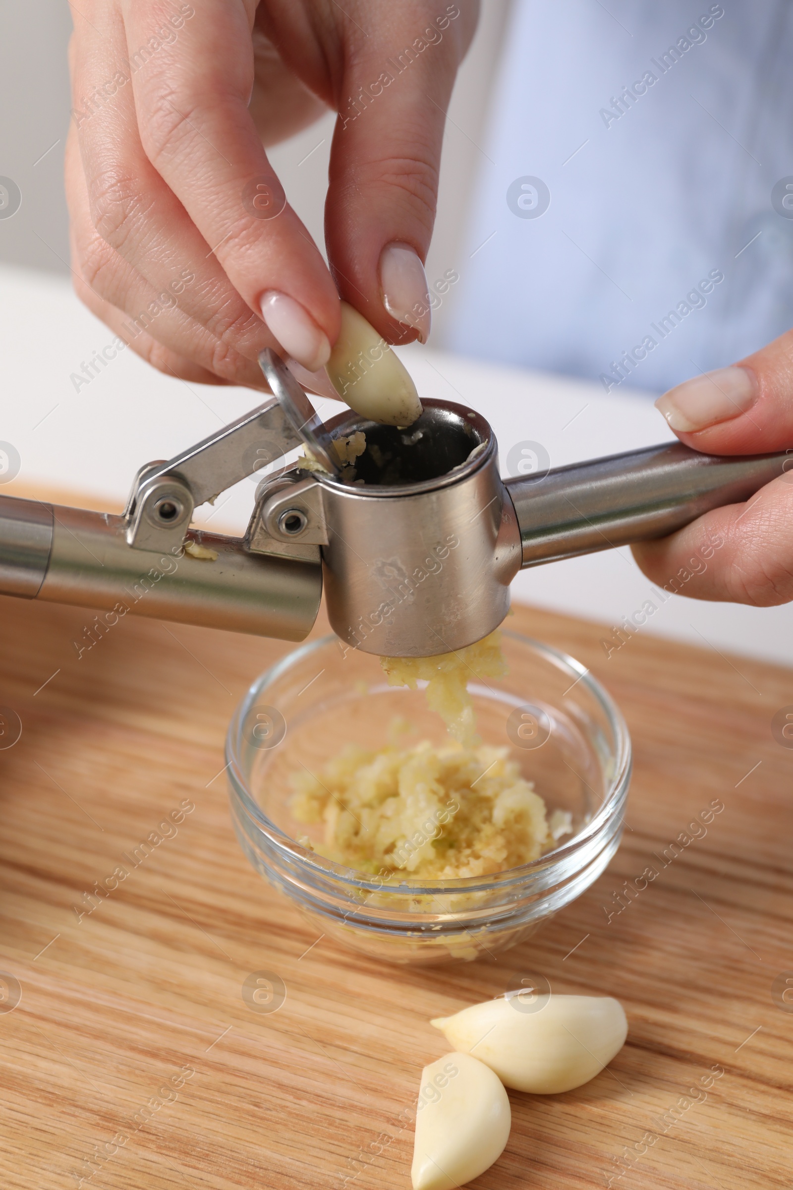 Photo of Woman squeezing garlic with press at wooden table, closeup