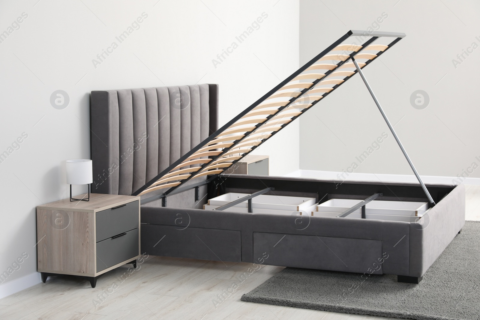 Photo of Comfortable bed with storage space for bedding under lifted slatted base in room