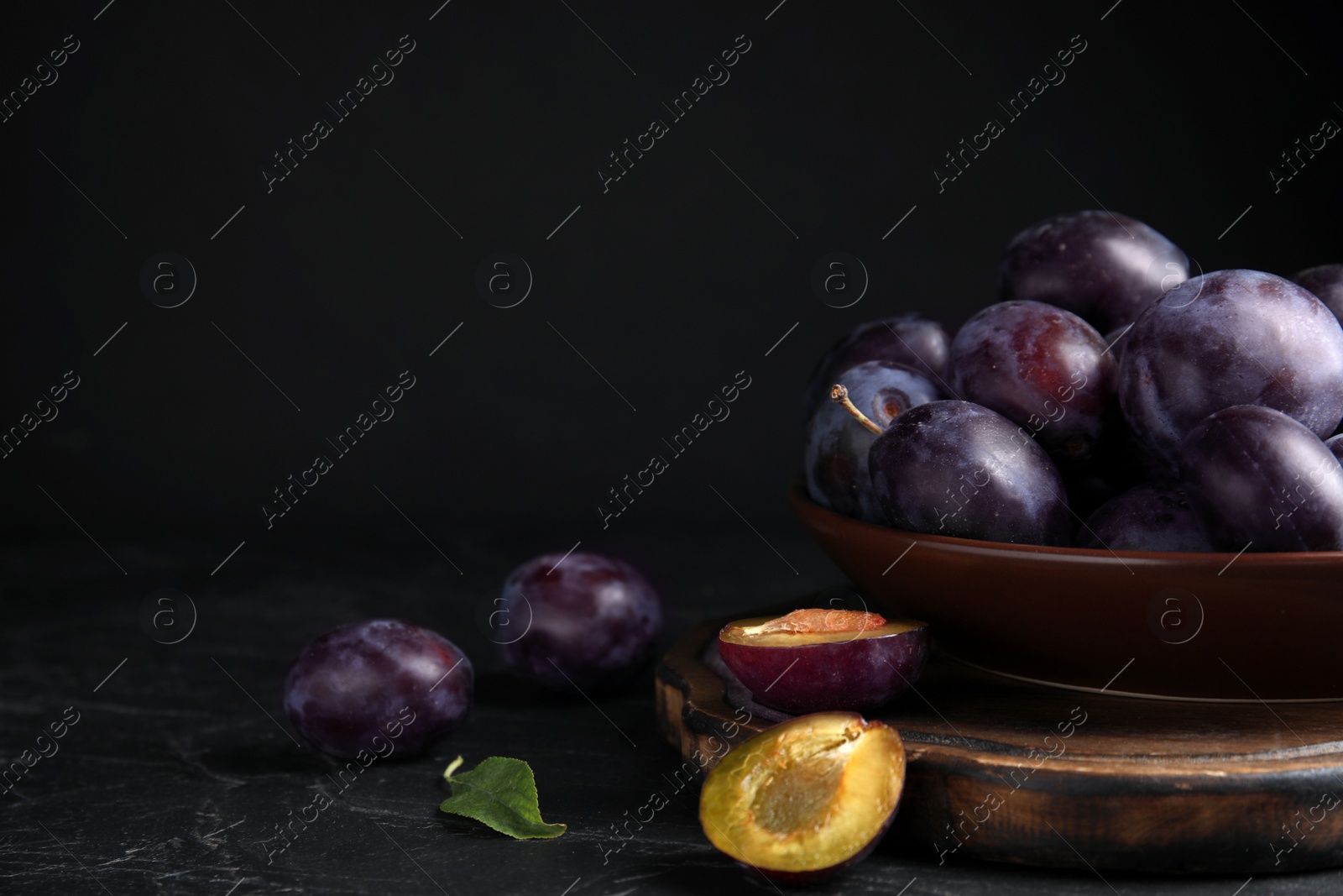Photo of Delicious ripe plums on table against black background. Space for text