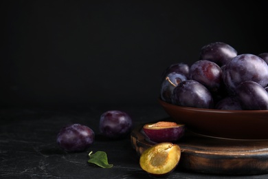 Delicious ripe plums on table against black background. Space for text