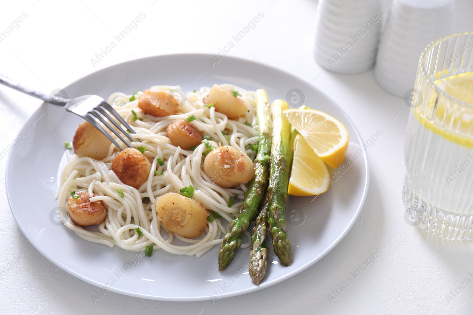 Photo of Delicious scallop pasta with asparagus, green onion and lemon served on white table, closeup