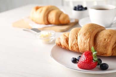 Plate with fresh crispy croissant and berries on white wooden table. Space for text