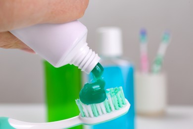 Photo of Woman applying paste on toothbrush against blurred background, closeup