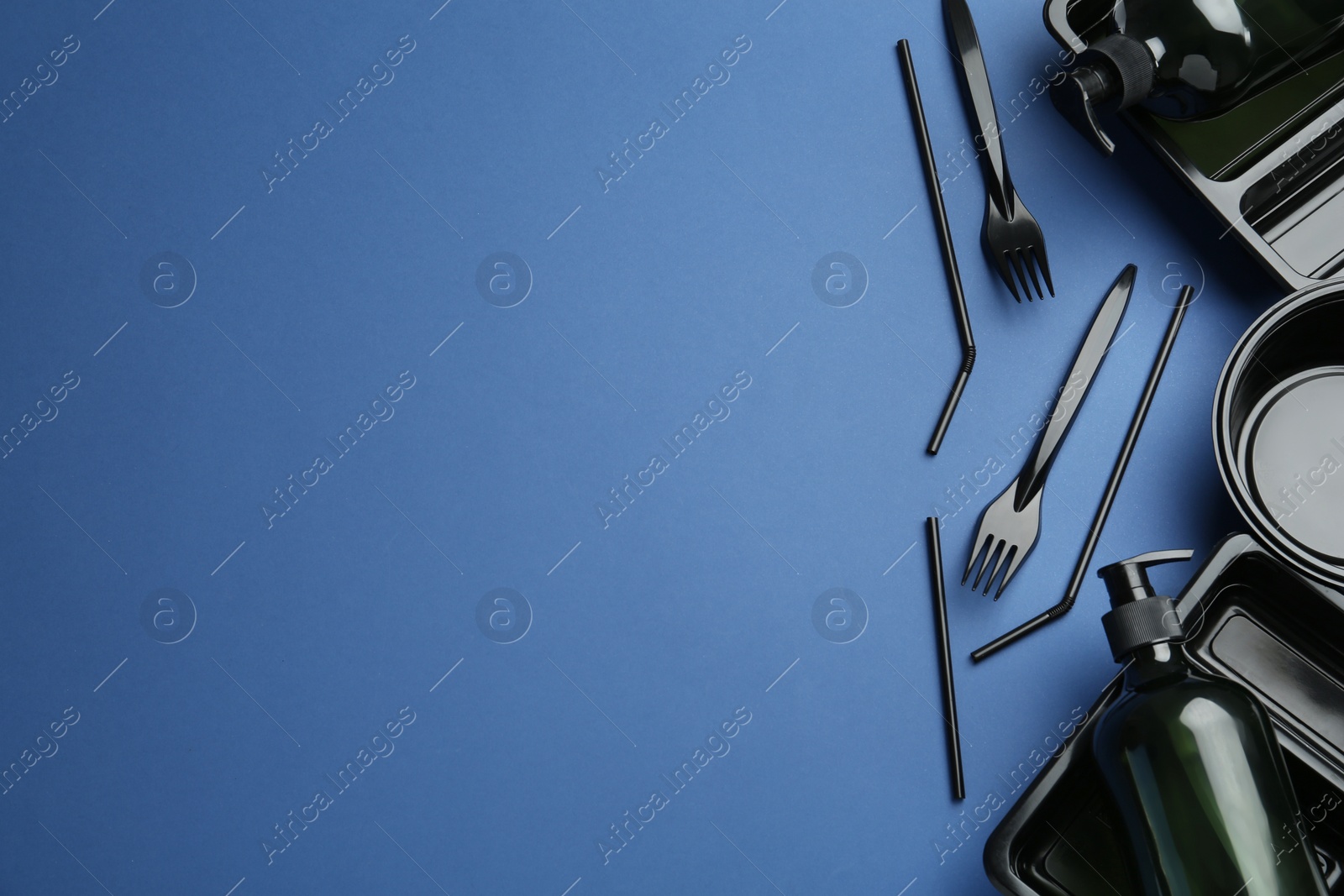 Photo of Plastic dishware and dispenser on blue background, flat lay. Space for text