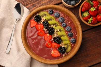 Bowl of delicious smoothie with fresh blueberries, strawberries, kiwi slices and blackberries on wooden table, flat lay