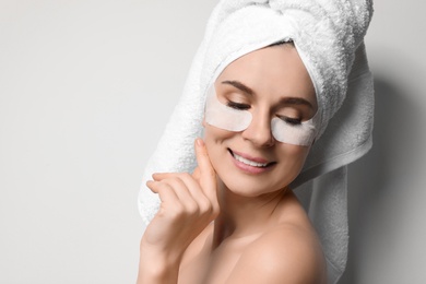 Photo of Beautiful woman with eye patches against light background, space for text. Facial mask