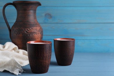 Clay cups with milk on light blue wooden table, space for text