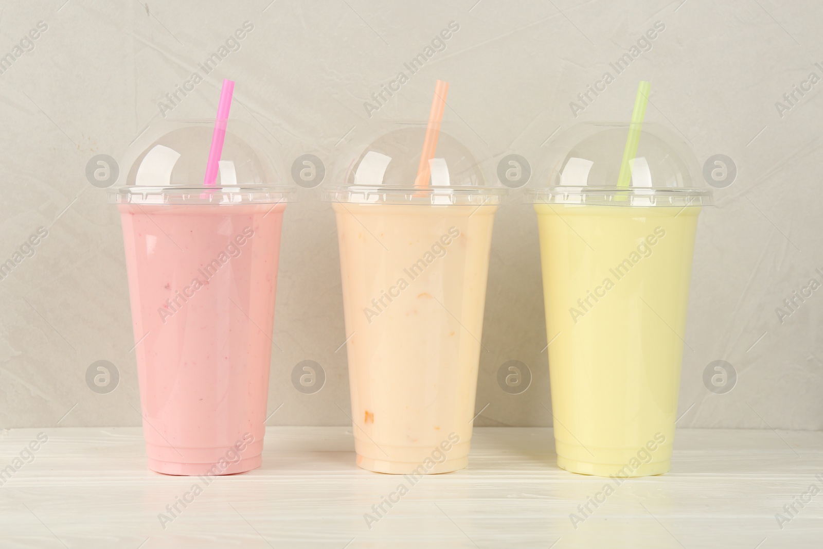 Photo of Plastic cups of different tasty smoothie on white wooden table