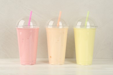 Plastic cups of different tasty smoothie on white wooden table