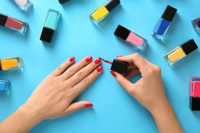 Photo of Woman applying bright nail polish on color background, top view