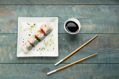 Photo of Delicious rolls wrapped in rice paper on light blue wooden table, flat lay
