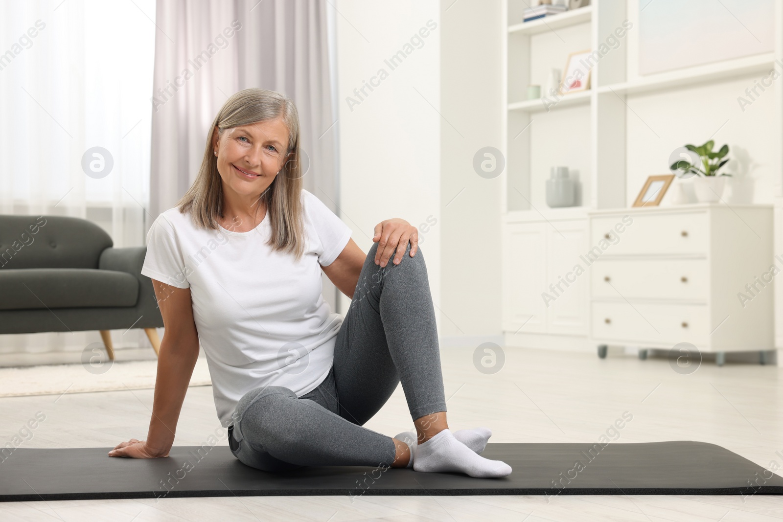 Photo of Happy senior woman sitting on mat at home, space for text. Yoga practice