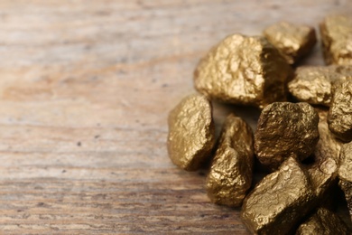 Photo of Pile of gold nuggets on wooden background. Space for text