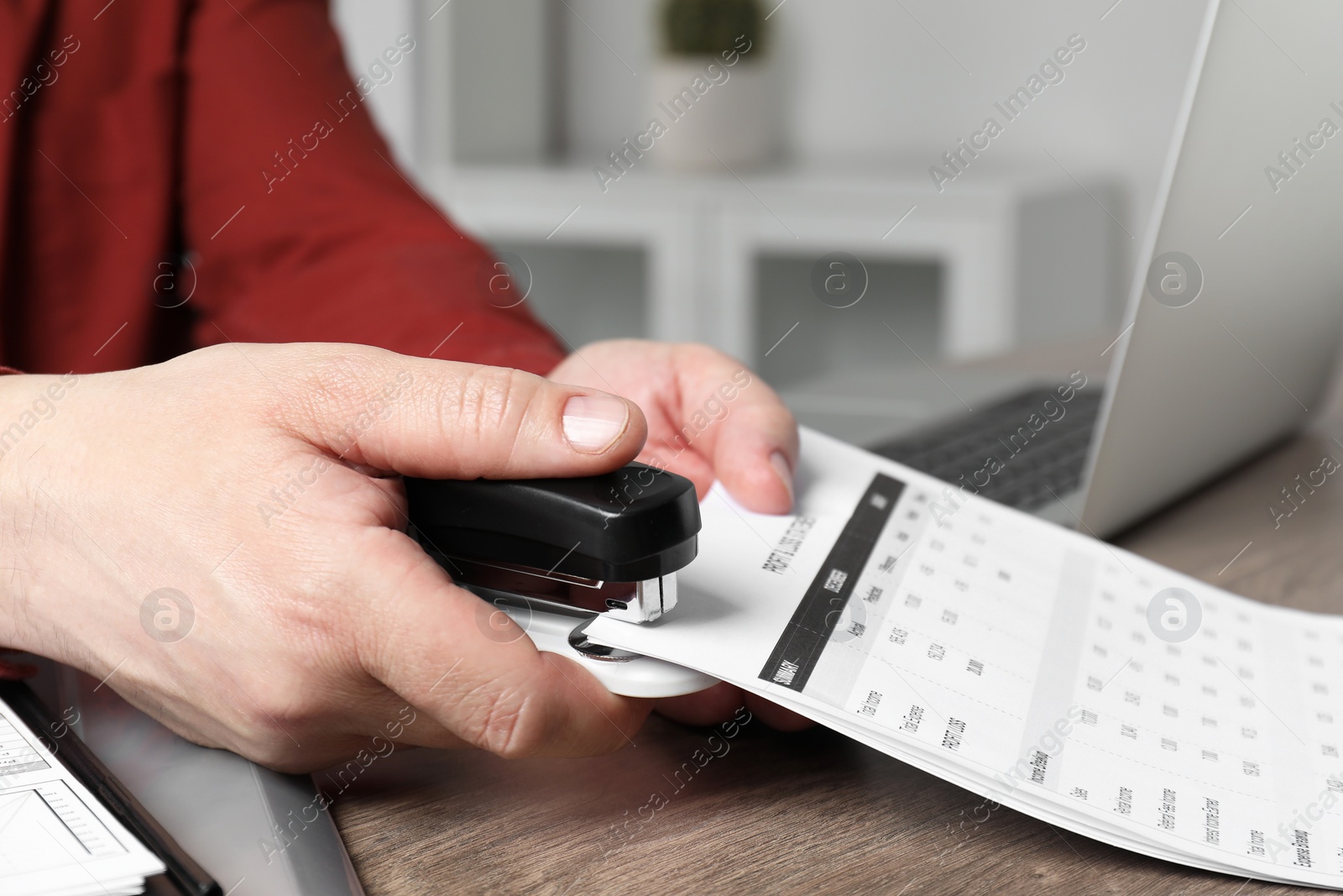 Photo of Man with documents using stapler at wooden table, closeup