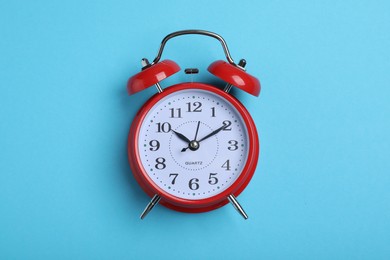 Alarm clock on light blue background, top view. School time