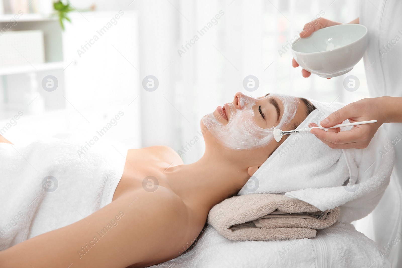 Photo of Cosmetologist applying mask on client's face in spa salon