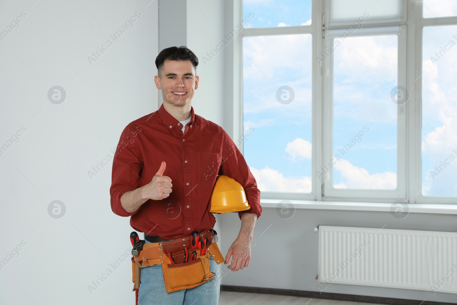 Photo of Handyman with hard hat and tool belt showing thumb up in empty room