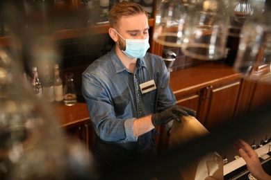 Photo of Waiter giving packed takeout order to customer in restaurant. Food service during coronavirus quarantine
