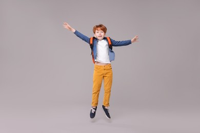 Photo of Happy schoolboy with backpack jumping on grey background