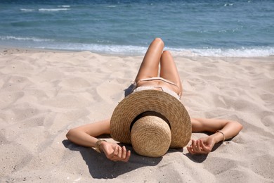Photo of Woman in bikini with straw hat lying on sandy beach near sea