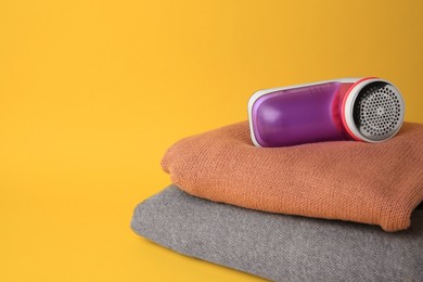 Photo of Modern fabric shaver and woolen clothes on yellow background. Space for text