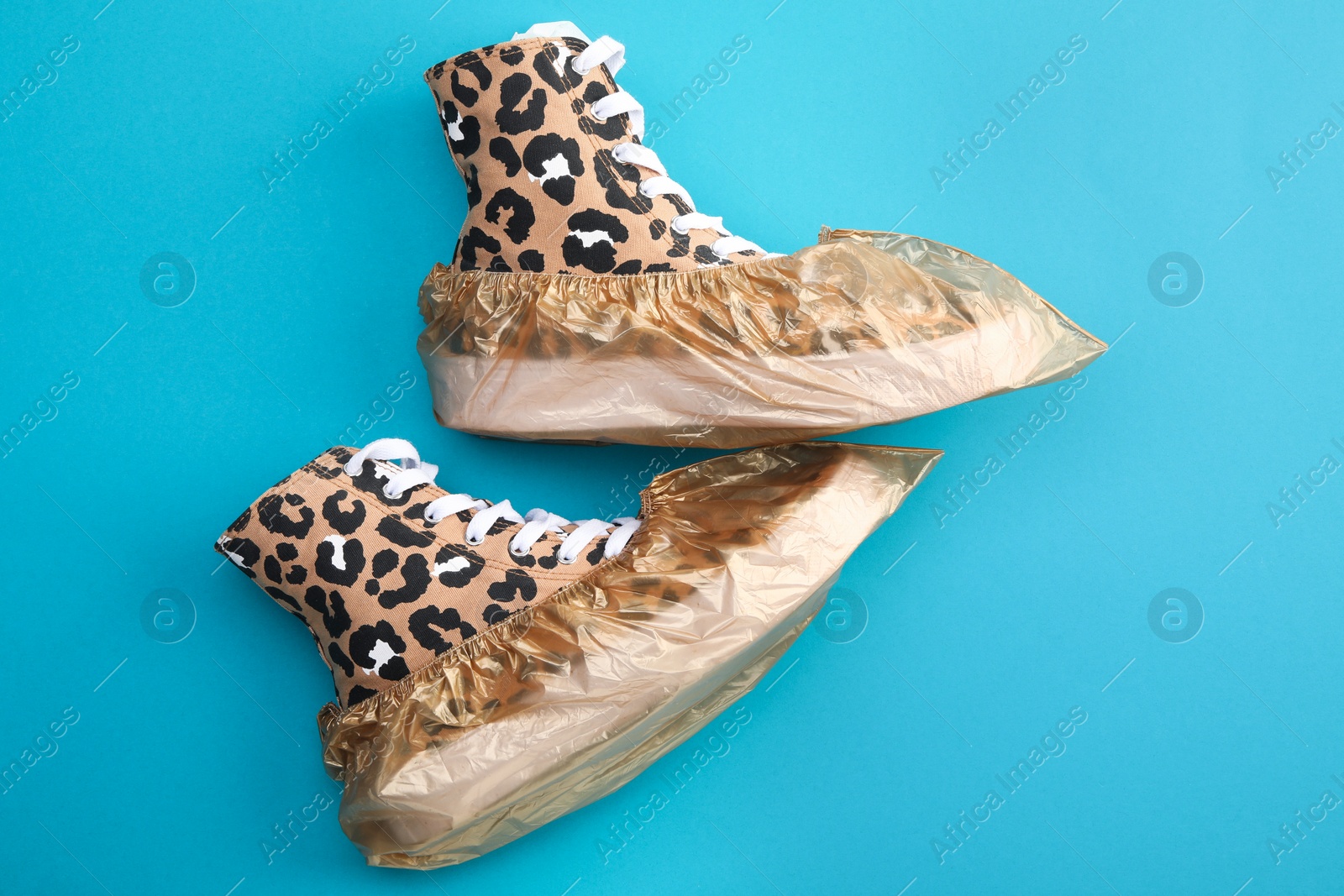 Photo of Sneakers in shoe covers on light blue background, top view