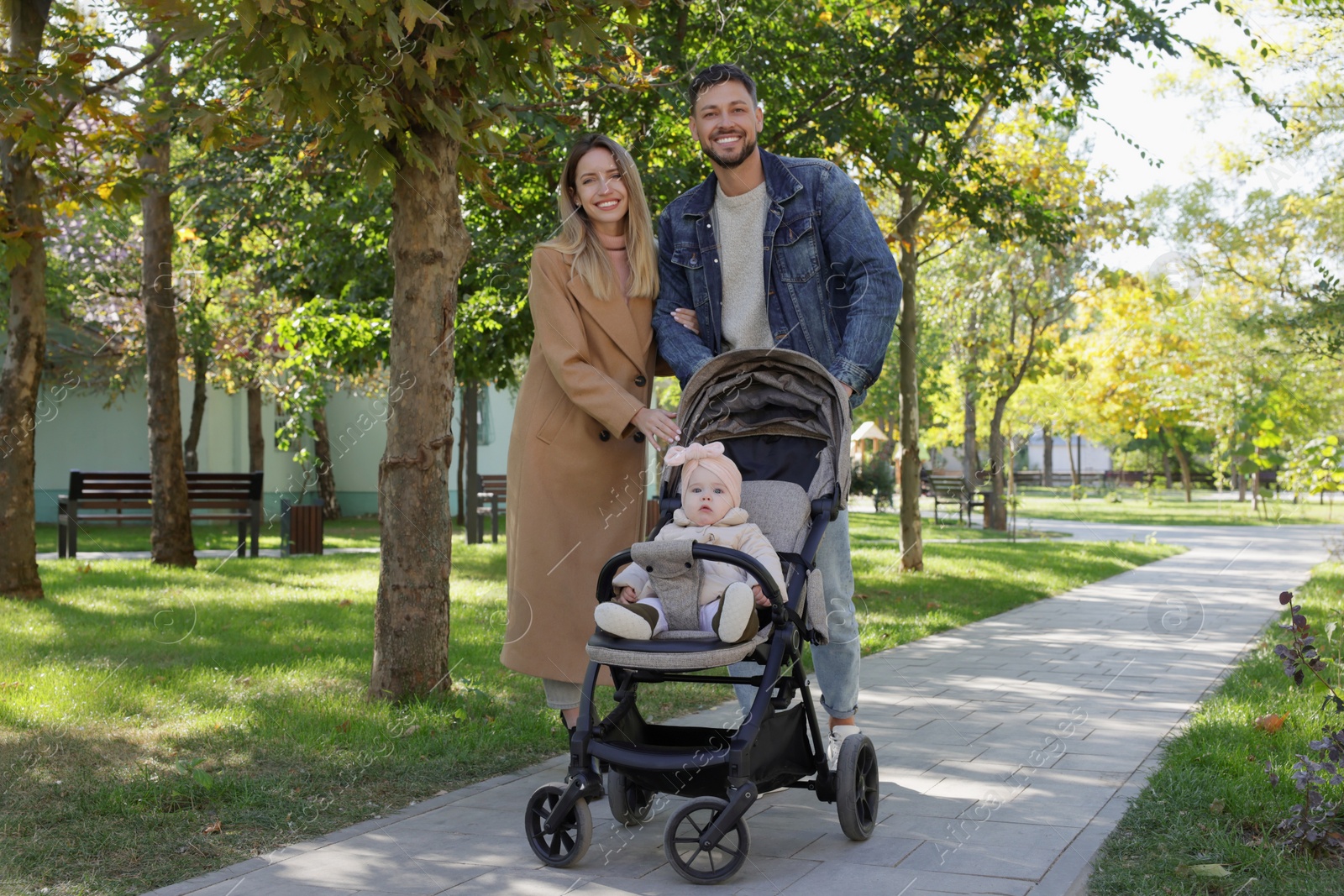 Photo of Happy parents walking with their baby in stroller at park on sunny day