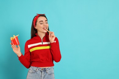 Beautiful young woman eating French fries on light blue background. Space for text