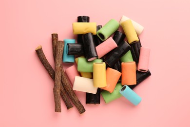 Photo of Many tasty candies and dried cut liquorice root on pink background, top view