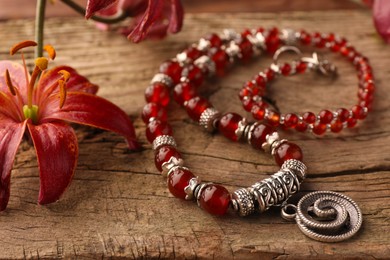 Beautiful necklace with gemstones and lily flowers on wooden surface, closeup