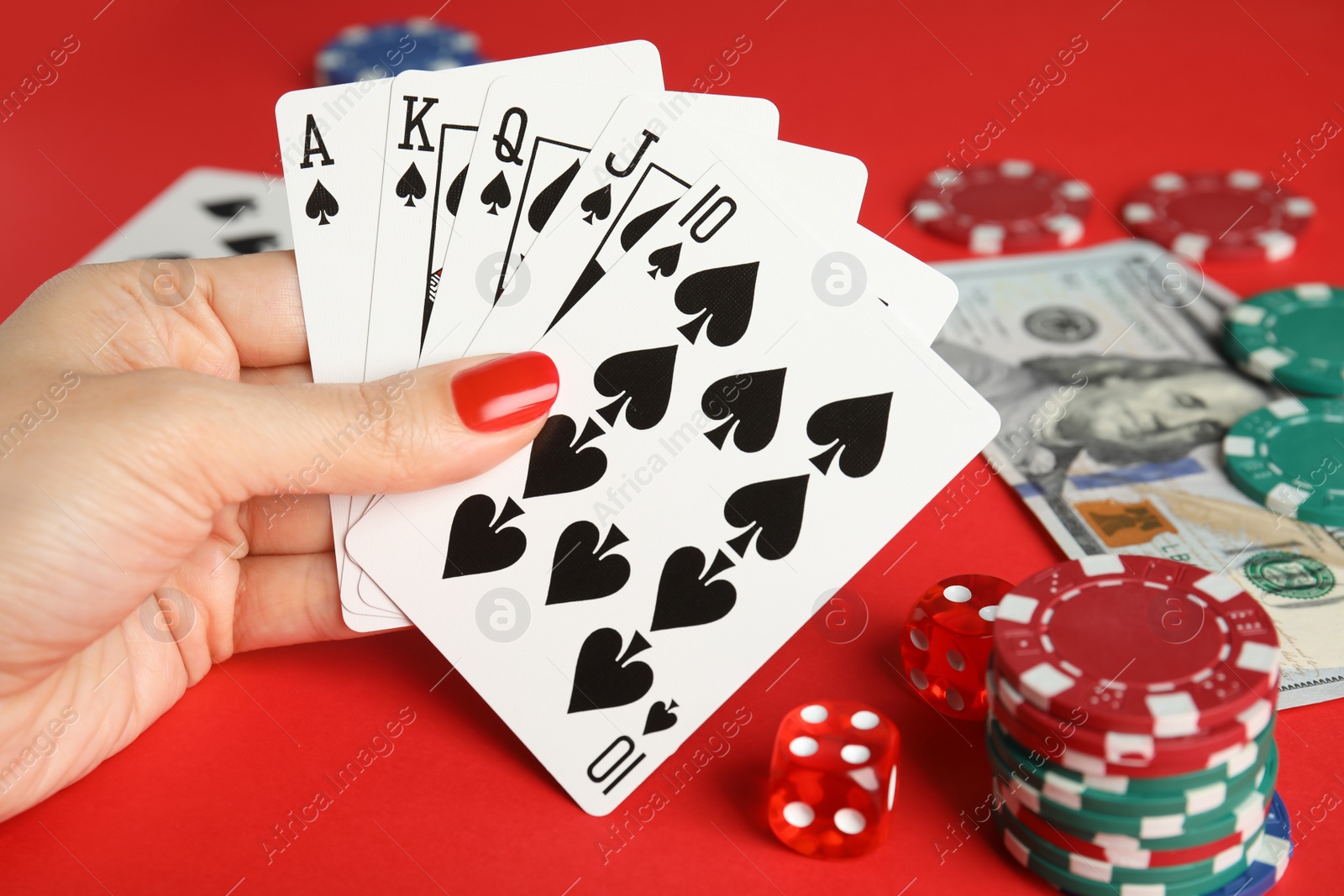 Photo of Woman holding playing cards with royal flush combination at red table, closeup