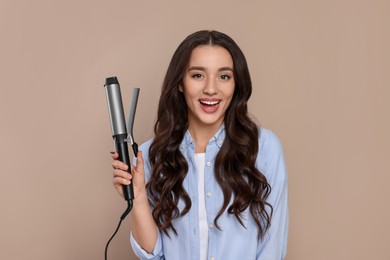 Happy woman with curling hair iron on beige background