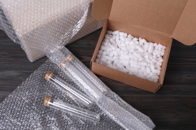 Photo of Test tubes with bubble wrap and cardboard box on dark wooden table, above view