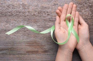 Photo of World Mental Health Day. Woman holding green ribbon on wooden background, top view