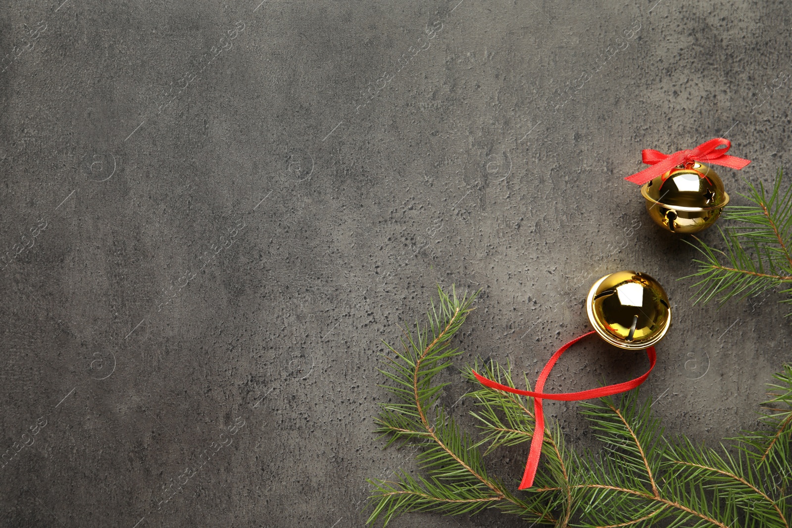 Photo of Golden sleigh bells and fir branches on grey background, flat lay. Space for text