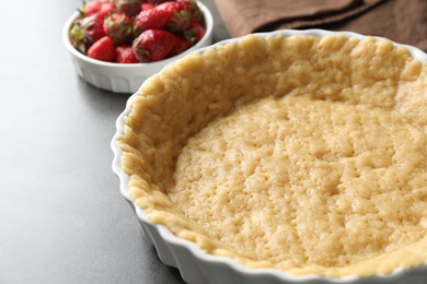 Photo of Making shortcrust pastry. Raw dough in baking dish and strawberries on grey table, closeup