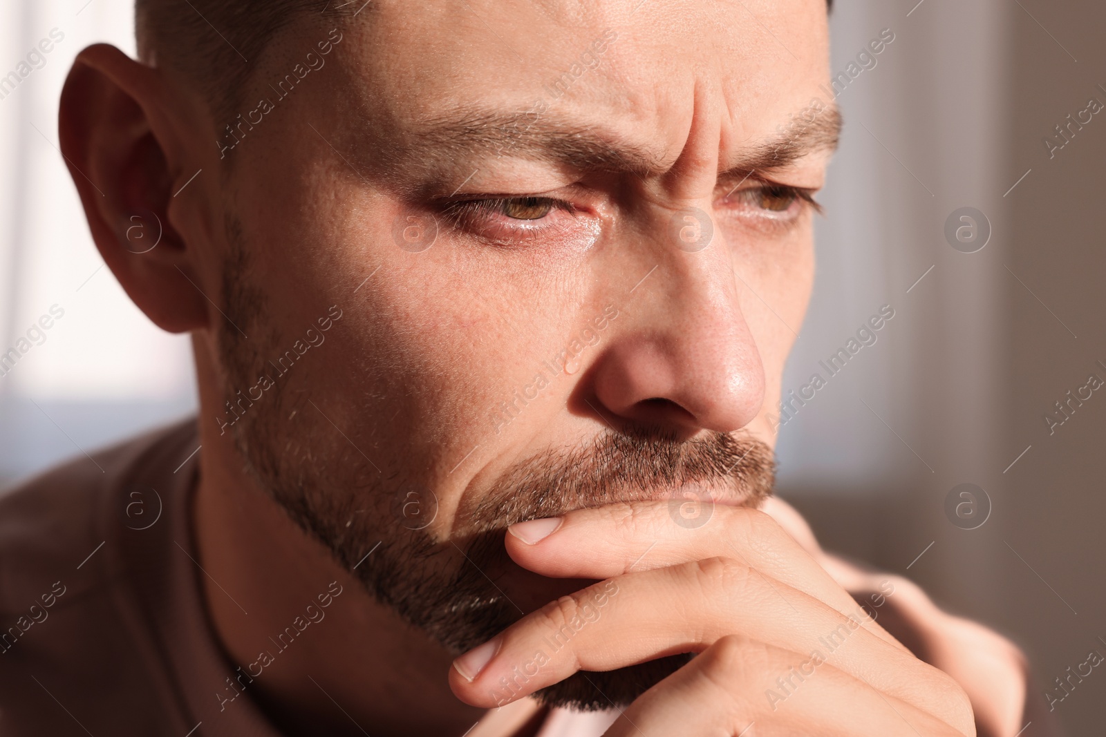 Photo of Upset man crying indoors, closeup. Loneliness concept