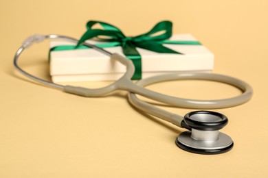 Photo of Stethoscope and gift box on beige background, closeup. Happy Doctor's Day