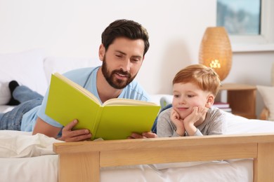 Photo of Father reading book with his child on bed at home