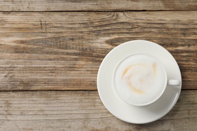 Photo of Tasty cappuccino in coffee cup on wooden table, top view. Space for text