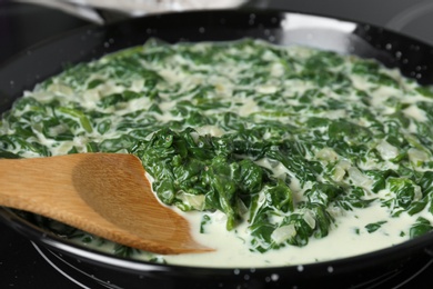 Photo of Tasty spinach dip with wooden spoon in frying pan, closeup view