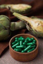 Photo of Bowl with pills and fresh artichokes on brown table, closeup