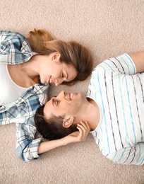 Photo of Lovely young couple lying on cozy carpet at home