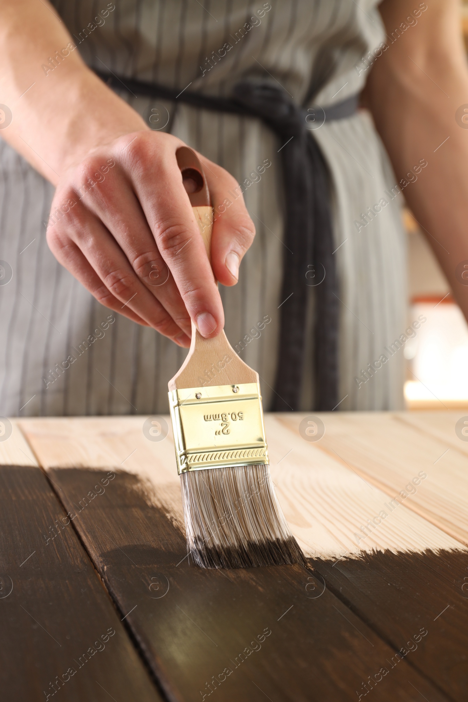 Photo of Man with brush applying wood stain onto wooden surface indoors, closeup