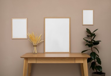 Photo of Empty frames, wooden table and plant near pale rose wall. Mockup for design