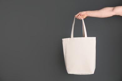 Photo of Man holding cotton shopping eco bag on grey background. Mockup for design