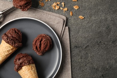 Chocolate ice cream scoops in wafer cones on gray textured table, flat lay. Space for text