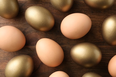 Photo of Golden eggs among others on wooden background, flat lay